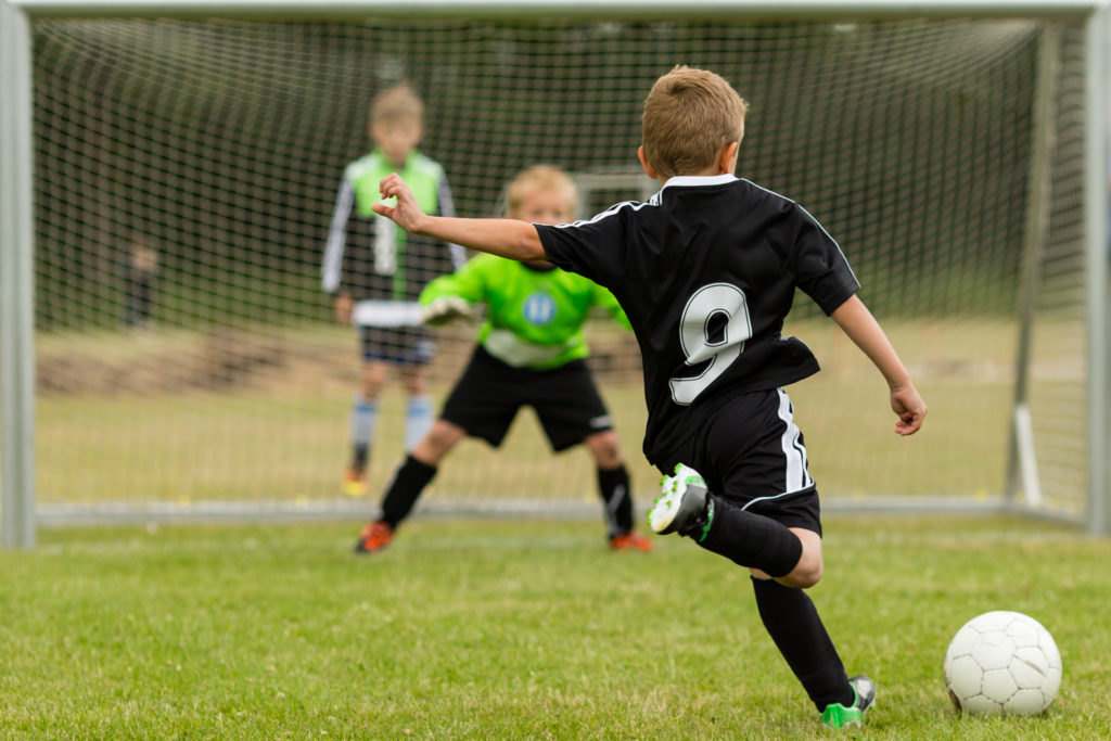Goalkeeper and penalty kicker in the midst of a penalty kick during a youth soccer match. Focus is on the kicker.